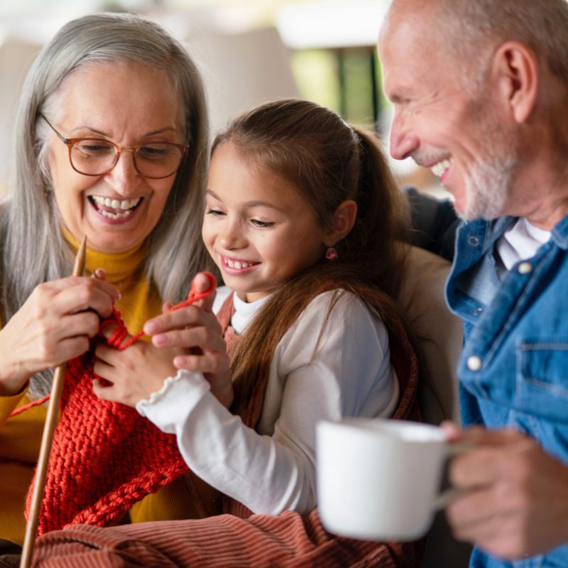 Little girl sitting on sofa with her grandparents and learning to knit indoors at home.; Shutterstock ID 2144837033; purchase_order: Customer contribution; job: 4706510; client: Sonova Australia ; other: Sonova