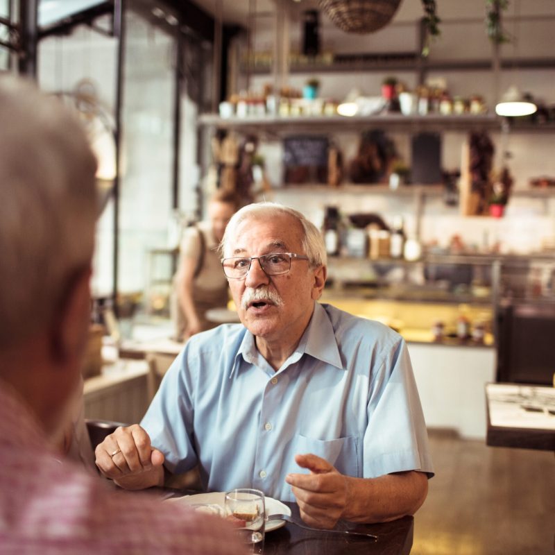 Two elderly men having a serious conversation in a restaurant; Shutterstock ID 2515090239; purchase_order: Customer contribution; job: 4706510; client: Sonova Australia ; other: Sonova