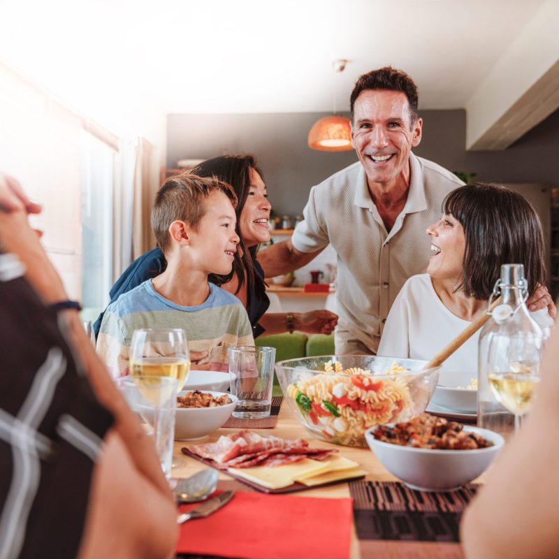 Family and friends reunion at home. Group of diverse family members laughing and having a good time while eating dinner at home enjoying their togetherness; Shutterstock ID 2725502167; purchase_order: Customer contribution; job: 4706510; client: Sonova Australia ; other: Sonova